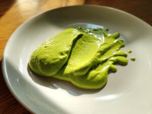 A vibrant smear of bright green avocado sauce on a light ceramic plate, highlighted by sunlight.