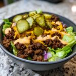 A close-up of an Amazing cheeseburger bowl featuring seasoned ground beef, shredded cheese, special sauce, and pickle slices over lettuce.
