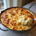 A spoonful of creamy, baked hot crab dip being lifted from a cast iron skillet with a golden-brown, cheesy top.