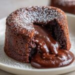 Close-up of a freshly baked chocolate lava cake with molten chocolate oozing out, dusted with powdered sugar.