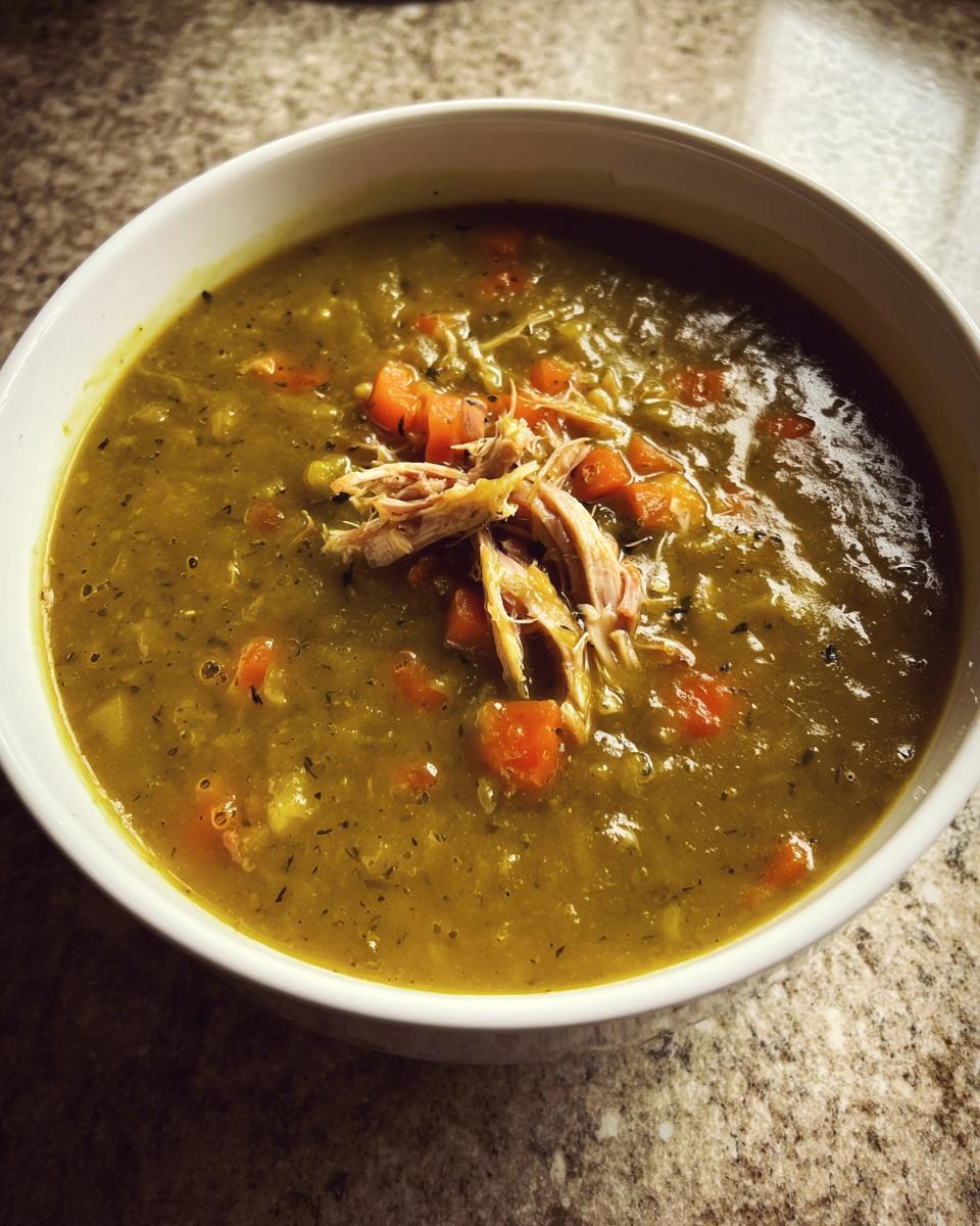 Close-up of a thick, green bowl of amazing pea soup topped with shredded chicken and diced carrots.