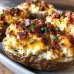 A close-up of a delicious twice baked potato stuffed with creamy filling, topped with melted cheddar cheese, crispy bacon bits, and fresh chives.