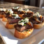 Close-up of several steak crostini bites topped with medium-rare steak, caramelized onions, and crumbled cheese.