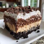 A rich, layered slice of Baileys Chocolate Cheesecake Trifle featuring a dark crust, light filling, chocolate mousse, whipped cream, and chocolate shavings.