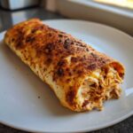 A single, golden-brown baked chimichangas filled with shredded chicken and melted cheese, served on a white plate.