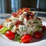 A mound of creamy BLT chicken salad served on lettuce and garnished with cherry tomatoes and crispy bacon bits.