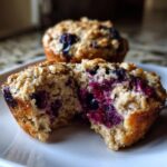 Close-up of a blueberry oatmeal muffin split in half, showing moist crumb and burst blueberries inside.