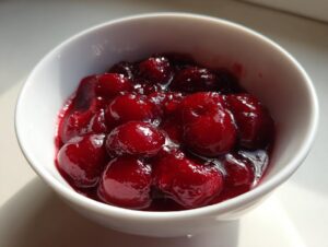 A close-up, bright photo of thick, glossy cherry pie filling made with whole cherries in a small white bowl.