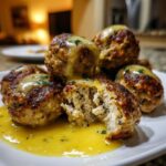 Close-up of browned chicken piccata meatballs covered in a bright yellow lemon sauce, one meatball is cut open.