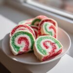 Close-up of festive red, green, and white pinwheel cookies dusted with sugar on a white plate.