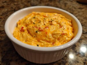 A close-up of creamy, bright orange cottage cheese queso dip topped with herbs and red pepper flakes in a white ramekin.