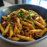 A close-up shot of a bowl filled with creamy beef pasta made with penne, topped generously with ground beef and fresh parsley.