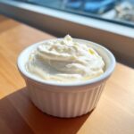 A close-up of thick, creamy horseradish sauce served in a small white fluted ramekin on a wooden surface.