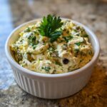 A close-up of a creamy, chunky olive dip, garnished with fresh parsley, served in a small white ramekin.