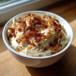 A white bowl filled with creamy onion dip, generously topped with crispy, caramelized onions.