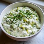 Close-up of a creamy, chunky pickle dip garnished with fresh chives and dill.
