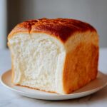A close-up of a freshly baked loaf of japanese milk bread, showing its incredibly soft white crumb and golden-brown top crust.