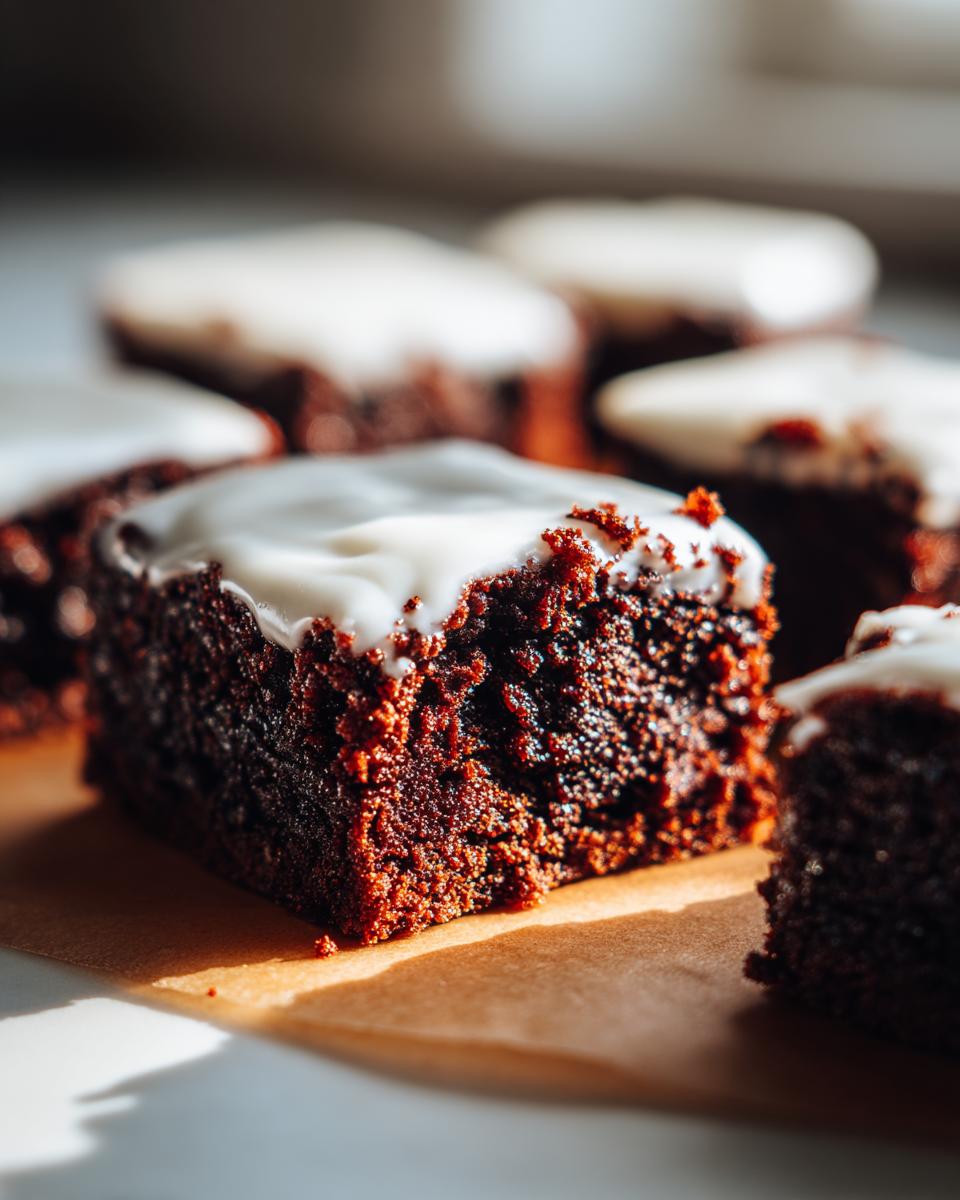 A close-up shot of a rich, dark gingerbread brownies square topped with thick white frosting.