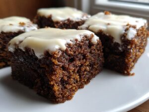 Close-up of four moist, dark gingerbread brownies topped with thick white frosting.