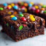 Close-up of a rich, fudgy cosmic brownie slice topped with chocolate glaze and colorful candy pieces.