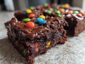 Close-up of a fudgy square of cosmic brownies topped with melted chocolate glaze and colorful candy pieces.
