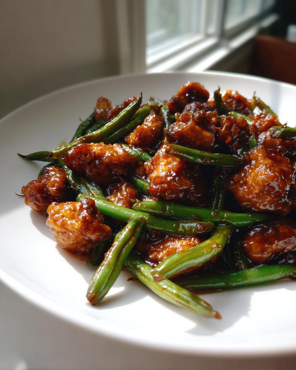 Close-up of glazed chicken and green beans dish served on a white plate, highlighting the rich sauce.