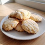 A close-up of several soft ricotta cookies drizzled with white glaze, stacked on a small white plate.