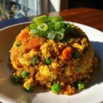 A mound of golden-colored cauliflower rice mixed with scrambled egg, peas, and carrots, topped with fresh green onions.