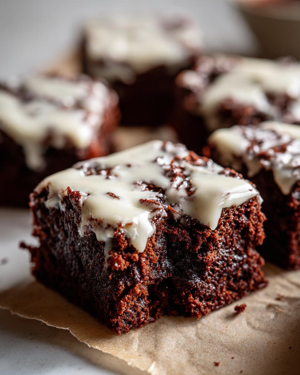 A close-up of a rich, dark square of gingerbread brownies topped with thick white icing.
