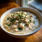 A close-up of a white bowl filled with creamy keto white chicken chili, topped with fresh chopped cilantro.