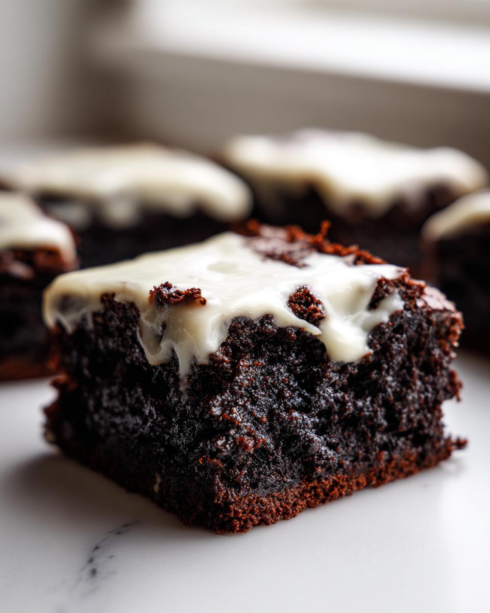 Close-up of a rich, dark gingerbread brownies square topped with white cream cheese frosting.