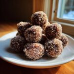 A close-up of a mound of dark, rich bourbon balls generously coated in sparkling sugar crystals on a white plate.