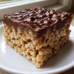 Close-up of a thick peanut butter rice krispie treats square topped with melted chocolate.