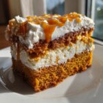 Close-up of a moist slice of pumpkin poke cake layered with cream filling and topped with whipped cream and caramel drizzle.