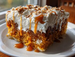 A moist slice of pumpkin poke cake soaked in caramel, topped with whipped cream and crumbs.