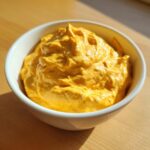 A close-up of thick, vibrant orange beer cheese dip served in a small white bowl on a wooden surface.