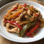 Close-up of shredded chicken mixed with colorful bell pepper strips, ready for crockpot chicken fajitas.
