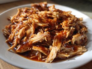 Close-up of shredded crockpot teriyaki chicken coated in a rich, glossy teriyaki sauce served on a white plate.
