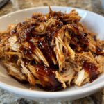 Close-up of shredded crockpot teriyaki chicken generously coated in glossy teriyaki sauce in a white bowl.