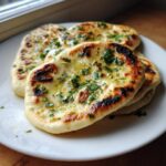 Close-up of soft, charred skillet naan bread recipe brushed with melted butter and sprinkled with fresh chopped cilantro.
