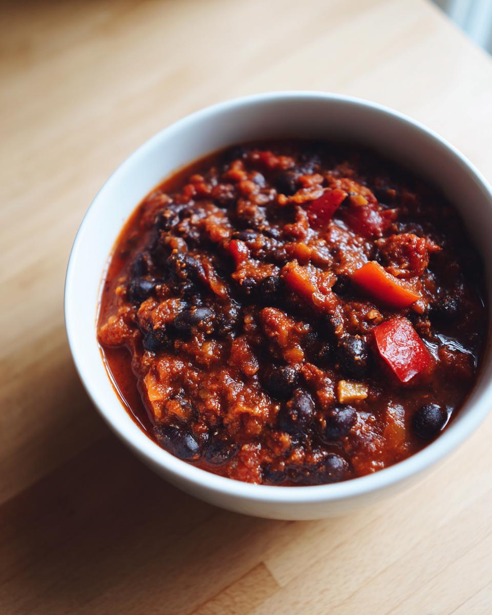 A close-up view of rich, thick black bean chili with visible chunks of tomato and red pepper in a white bowl.