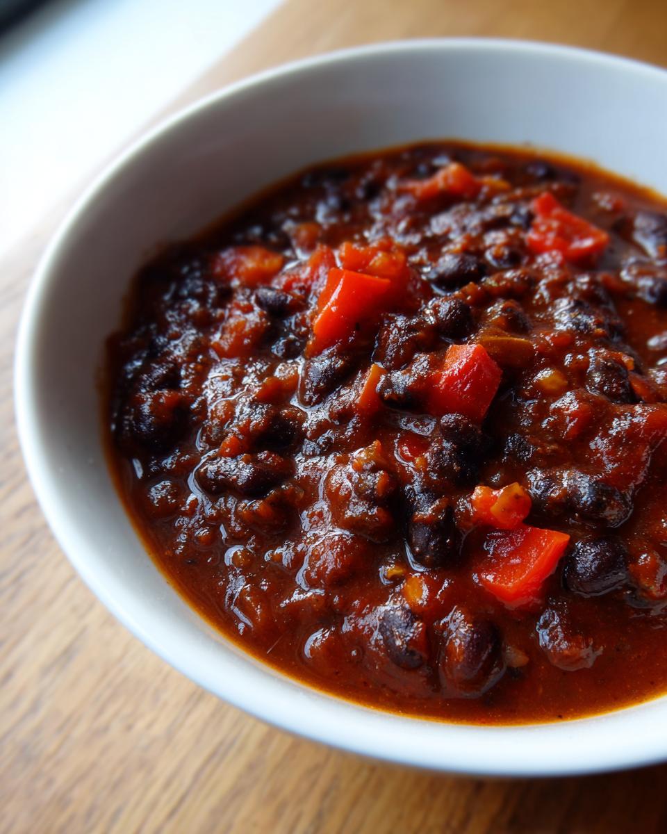 Close-up of a white bowl filled with rich, thick black bean chili featuring visible chunks of red pepper.