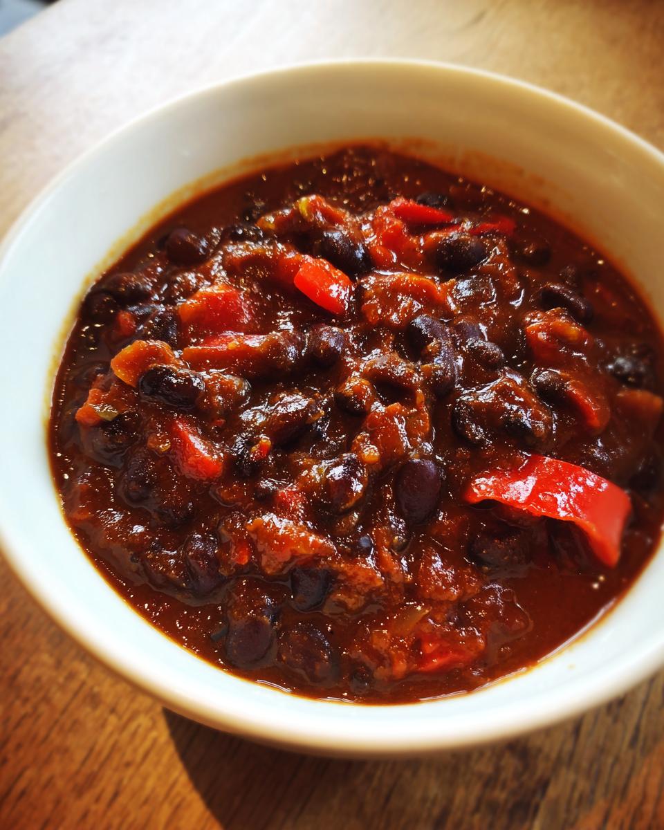 Close-up of a hearty bowl of smoky black bean chili with visible red peppers.