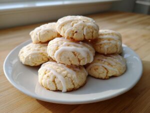 A stack of soft, pale ricotta cookies drizzled with a thin white glaze, resting on a white plate.