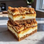 Two stacked apple cheesecake bars showing a thick graham cracker crust, creamy filling, apple layer, and crumb topping.