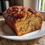 A freshly baked loaf of sweet Alabama pecan bread with a shiny, glazed pecan topping, sitting on a white plate.