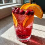 Close-up of a fizzy, red Thanksgiving punch garnished with fresh cranberries and orange slices, sitting in sunlight.