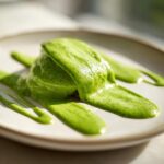 Close-up of a thick, vibrant green avocado sauce artfully drizzled and pooled on a light-colored plate.