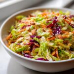 Close-up of a vibrant cabbage salad featuring shredded green and purple cabbage, carrots, almonds, and sesame seeds.