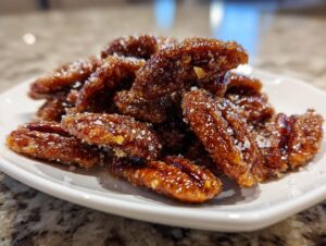 A pile of glistening, homemade candied pecans coated in a sweet, sugary glaze and coarse salt crystals.